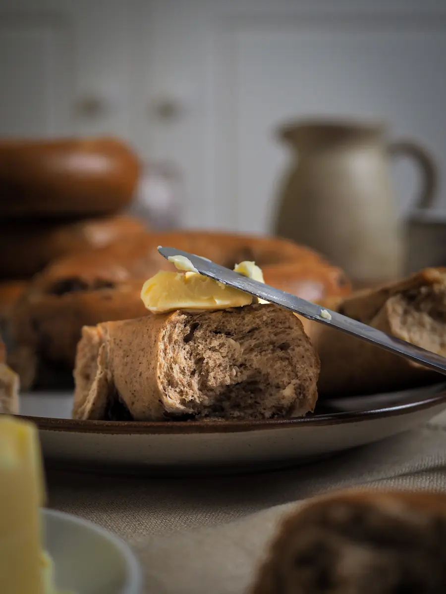 Sliced bagel topped with a spread of butter and a knife, set against a rustic kitchen background