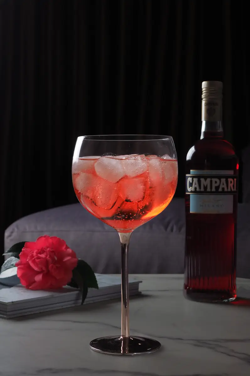 A vibrant red Campari cocktail served over ice in a balloon glass