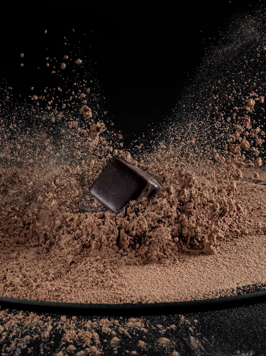 Dark chocolate square splashing into a pile of cocoa powder, creating a dramatic dust explosion effect