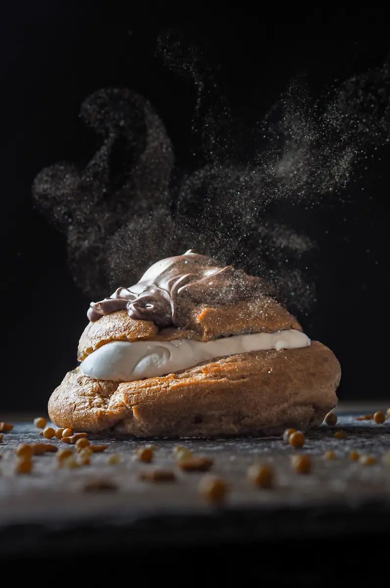 Gourmet chocolate cream puff with dramatic lighting and cocoa powder dusting on a slate surface
