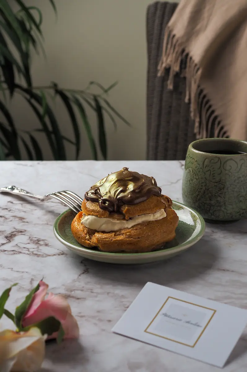 Gourmet choux pastry with edible gold and chocolate ganache plated in a cozy afternoon tea