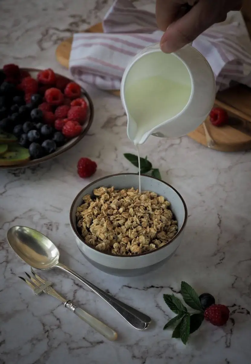 Pouring milk into a bowl of granola with fresh berries